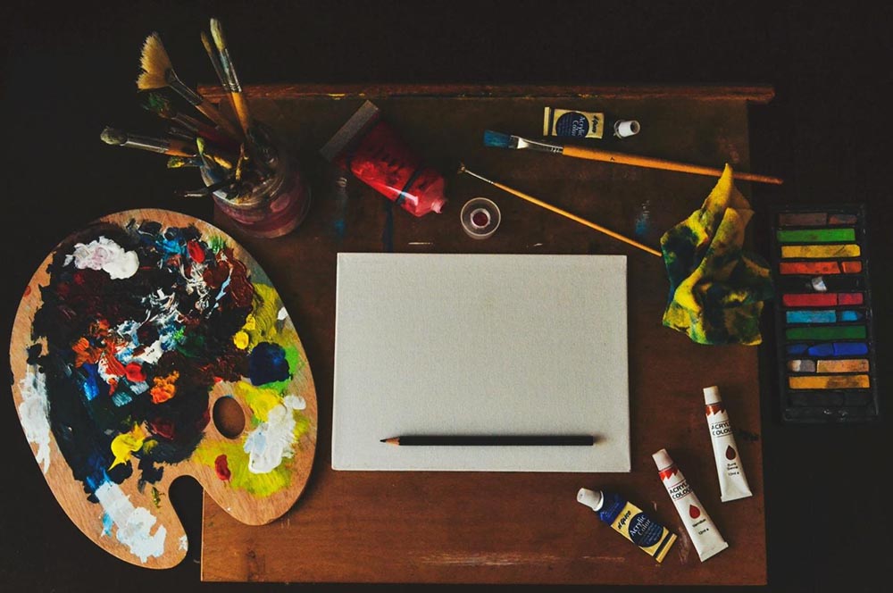 Downview photo of an artists desk, with a clean canvas and painting supplies.